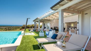 Un espace aménagé au bord de la piscine, avec des chaises longues, une pergola et une vue sur l’océan.