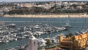 A marina with numerous boats docked, a beach with people in the background, and a building with a tower in the foreground. - Ocean view - 150 m beach - refurbished 4 to 6 places in Praia da Rocha 95 M2 (Portimão)