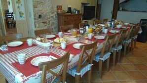 Zona de dinar amb una taula llarga preparada per l'esmorzar, amb plats, tasses i un plat de fruita.