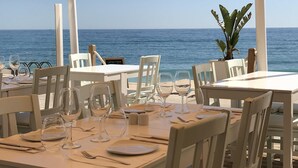 Un espace extérieur aménagé pour les repas, avec des tables et des chaises, offrant une vue sur la mer.