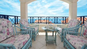 Ein Balkon mit Korbstühlen und einem Tisch, mit Blick auf die Küste.