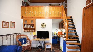 Ein gemütliches Wohnzimmer mit Fernseher, Holzmöbeln, einem blauen Sofa und einer Treppe, die in eine obere Ebene führt.
