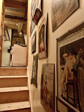 A staircase leading to a room with wooden beams, a white couch, and various framed artworks on the walls.
