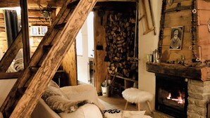 A cozy living room with a white sofa, a stone fireplace, and a rustic wooden ceiling. - Chalet Plagne (1800) (Mâcot-la-Plagne)