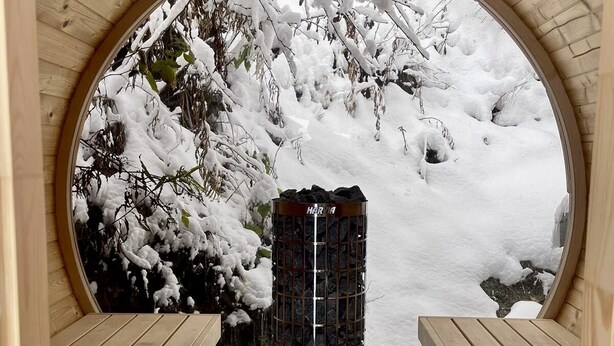 A sauna with a wooden bench and a view of a snowy landscape through a semi-circular window. - Chalet Plagne (1800) (Mâcot-la-Plagne)