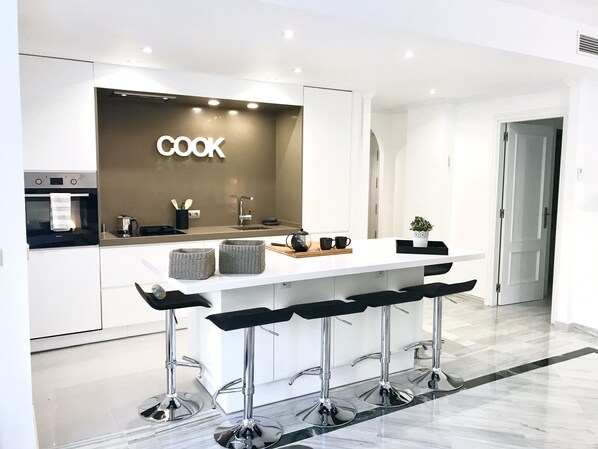 A modern kitchen with a central island, bar stools, and a coffee machine.