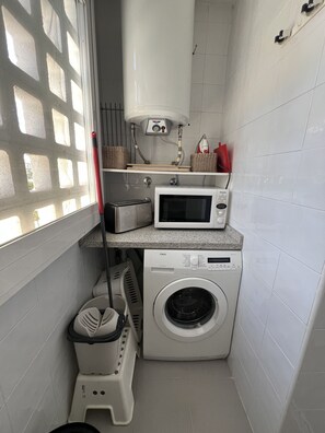 Une petite buanderie équipée d’un lave-linge, d’un four à micro-ondes et d’un grille-pain.