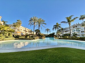 Ein Swimmingpool, umgeben von gepflegtem Rasen und Palmen, mit mehrstöckigen Gebäuden im Hintergrund.