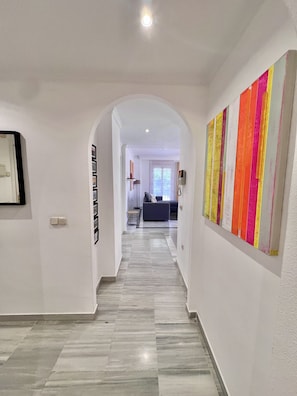 Un couloir doté d’un sol carrelé, de murs blancs et d’un tableau abstrait aux couleurs vives sur le mur de droite.