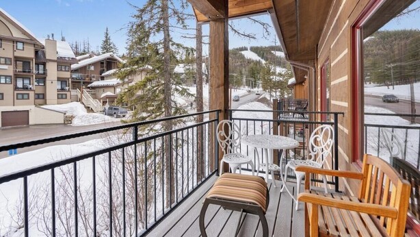 Un balcón de madera con mesa y sillas, con vistas a un paisaje nevado con edificios y árboles.