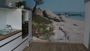 A kitchen with a large beach mural on the wall, a microwave, and a cabinet with a bowl of fruit. - House / Villa - FouesnantHouse with garden (Fouesnant)