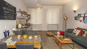Een moderne woonkamer met een eethoek, een kitchenette en een prikbord aan de muur met Wi-Fi en contactgegevens.