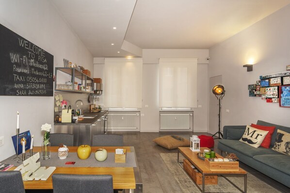 Un salon moderne comprenant un coin repas, une kitchenette et un tableau noir fixé au mur, avec accès Wi-Fi et coordonnées.