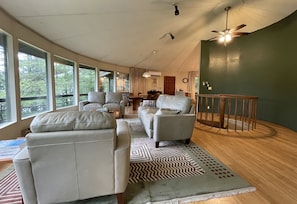 A spacious living area with a large window, a ceiling fan, and a dining area.