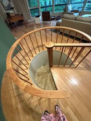 A wooden spiral staircase with a handrail, leading to a lower level.