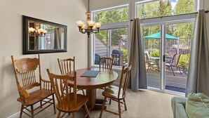 A dining area with a round table and wooden chairs, a chandelier, and a large window with a view of an outdoor patio.
