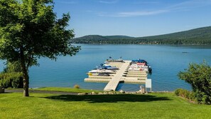 Un muelle con barcos, una zona con césped y un lago con colinas al fondo.
