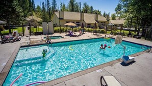 A swimming pool with a diving board, lounge chairs, and a fenced area with a building in the background.