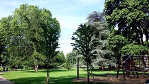 Um parque com um parquinho, um caminho pavimentado e várias árvores.
