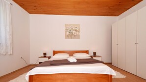 A bedroom with a wooden bed, white walls, a painting above the bed, and a wardrobe to the right. - DOROTEA 1, 3-room apartment for 6 persons, 50m from the pebble beach (Okrug Gornji)