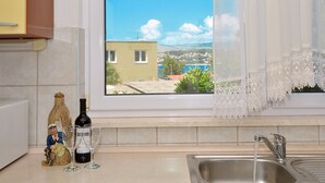 A kitchen with a window view of a coastal town, a sink, and decorative items. - DOROTEA 1, 3-room apartment for 6 persons, 50m from the pebble beach (Okrug Gornji)