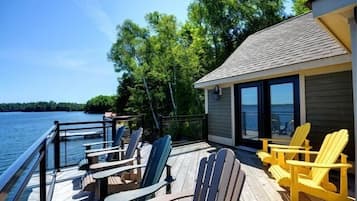 A deck with Adirondack chairs and tables overlooking a lake, with a building adjacent to the deck.