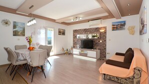 Ein modernes Wohnzimmer mit einer Couch, einem Esstisch, Stühlen und einem Fernseher.