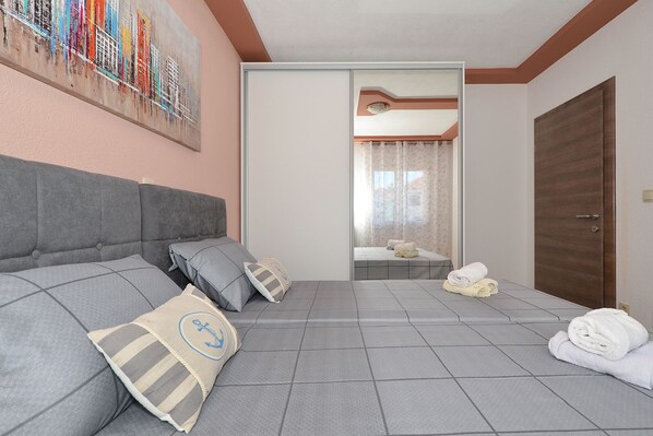 A hotel room with a grey sofa, a bed with a white headboard, a wooden door, and a painting on the wall. - ARTE, spacious apartment with sea view, 4 + 1 persons, 80m from pebble beach (Seget Donji)