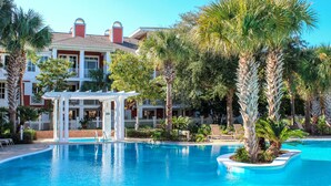 A pool area with a white gazebo, palm trees, and a building with balconies in the background.