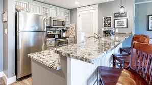 A modern kitchen with stainless steel appliances, a marble island, and wooden bar seating.