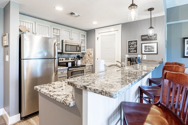 A modern kitchen with stainless steel appliances, a marble island, and wooden bar seating.