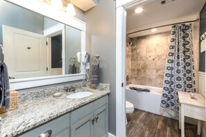 A bathroom with a granite countertop, a sink, a mirror, a shower with a patterned curtain, and a bathtub. - Charming Baytowne Wharf 1BR/2BA + Bunk Room — Steps to Village (Destin)