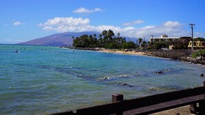 A beach with clear blue water, a rocky shoreline, and a mountain in the background.