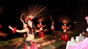 A group of performers in traditional costumes with feathered headdresses, performing on a stage with a table set for an event.