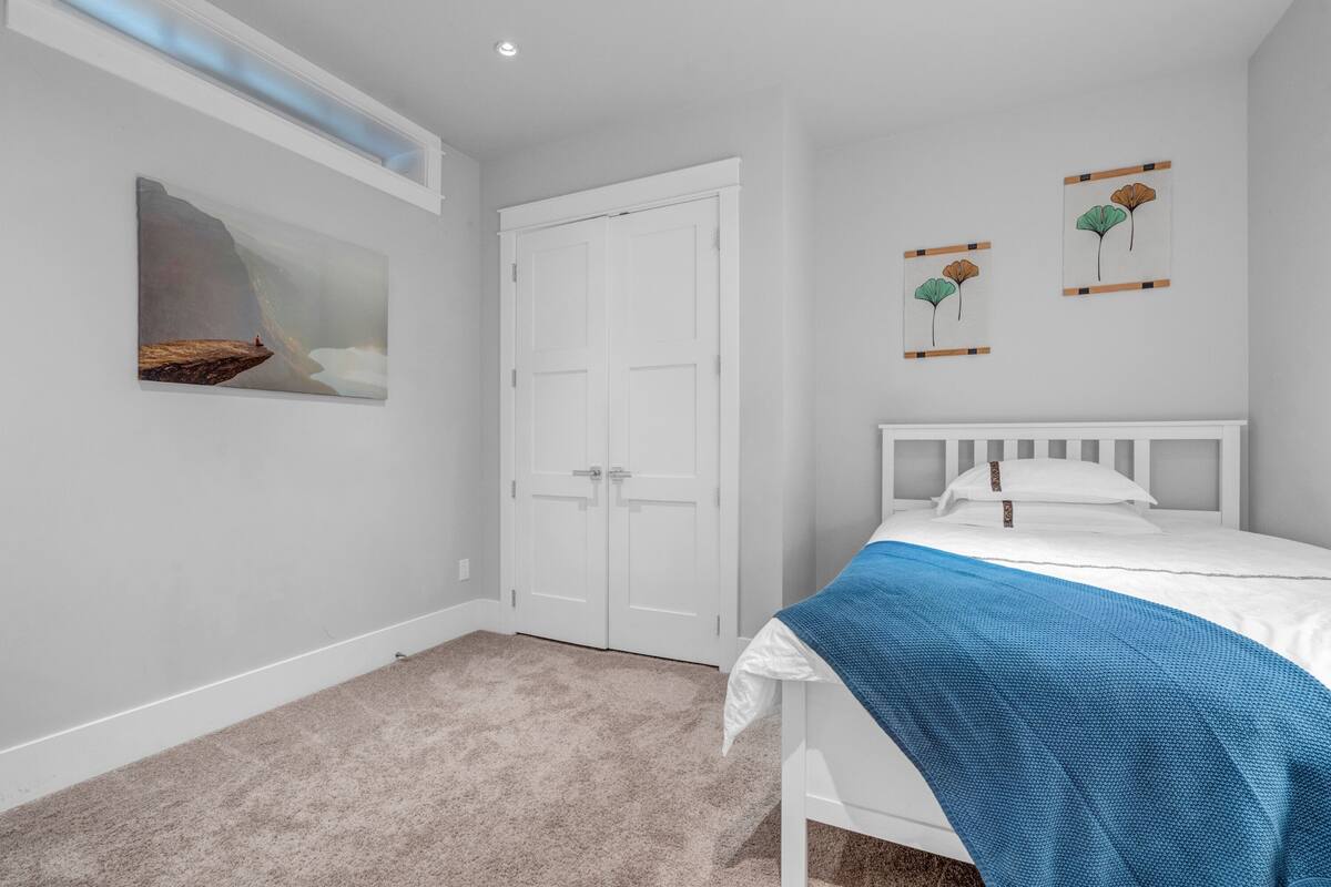 A bedroom with a white bed, a blue blanket, a white door, and two wall art pieces.