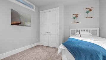 A bedroom with a white bed, a blue blanket, a white door, and two wall art pieces.