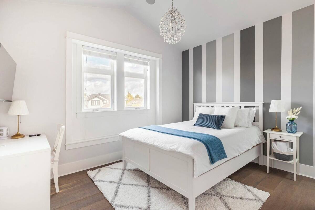 A modern bedroom with a white bed, a nightstand, a desk, and a large window.