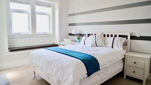 Een net opgemaakt bed met een blauwe plaid, witte lakens en een nachtkastje met een lamp.