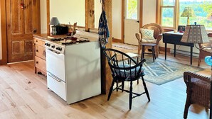 Une cuisine rustique avec un poêle, un coin repas avec des chaises en osier et une vue sur l’extérieur.