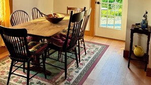 Un coin repas avec une table en bois, des chaises, un lustre et une porte donnant sur un jardin.