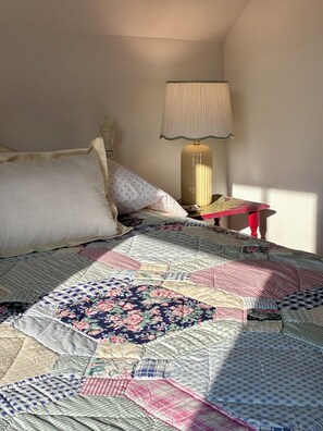 Un lit avec une couette, une lampe et une petite table.