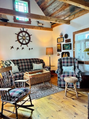 Un salon chaleureux avec un plafond en bois, un fauteuil à bascule, un canapé à carreaux et une chaise avec un siège en osier.
