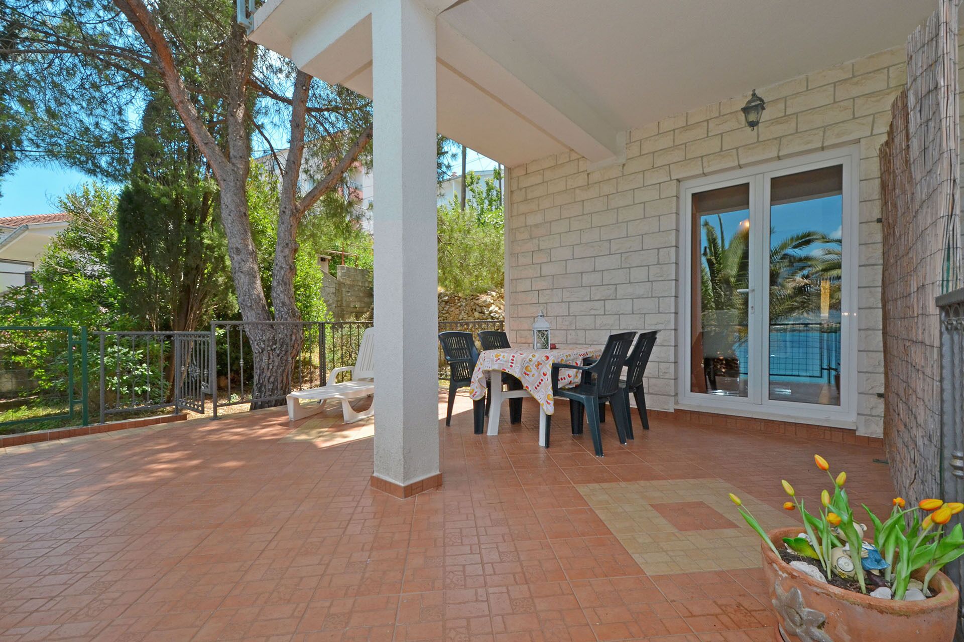 An outdoor patio with a table and chairs, a potted plant, and a view of a swimming pool.