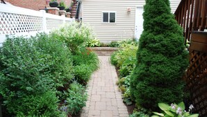 A narrow brick pathway flanked by lush greenery and a white fence. - Roscoe Village Inn -Guesthouse - Walk to Chicago's Wrigley Field (Chicago)