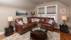 A living room with a brown leather sectional sofa, a glass coffee table, and two side tables with lamps. - Roscoe Village Inn -Guesthouse - Walk to Chicago's Wrigley Field (Chicago)