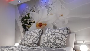 A bedroom with a bed, two patterned pillows, a large white flower arrangement, and a wall-mounted light fixture. - Vacation apartment Meyer with private pool and garden sauna, exclusive FEWO. (Mähren)