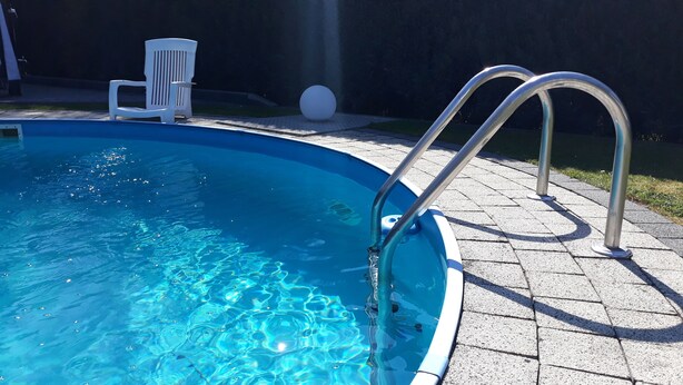 A swimming pool with metal ladders, a white chair, and a large white ball on the patio. - Vacation apartment Meyer with private pool and garden sauna, exclusive FEWO. (Mähren)