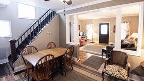 A spacious living area with a wooden dining table and chairs, a staircase, and a cozy seating area with a patterned armchair. - Charming, spacious home near towncenter amenities, resturants, trails and parks. (Middlebury)