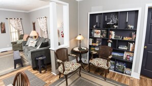 A living room with a sofa, two chairs, a small table, a bookshelf, and a door. - Charming, spacious home near towncenter amenities, resturants, trails and parks. (Middlebury)