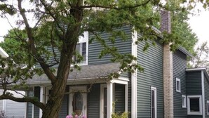 A two-story house with a prominent tree in the front yard. - Charming, spacious home near towncenter amenities, resturants, trails and parks. (Middlebury)